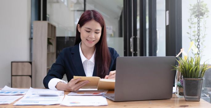 Charming asian businesswoman sitting working on laptop in office..