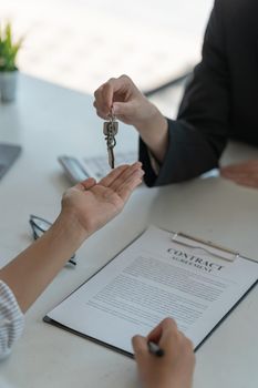 real estate agent holding house key to his client after signing contract agreement in office,concept for real estate, moving home or renting property.