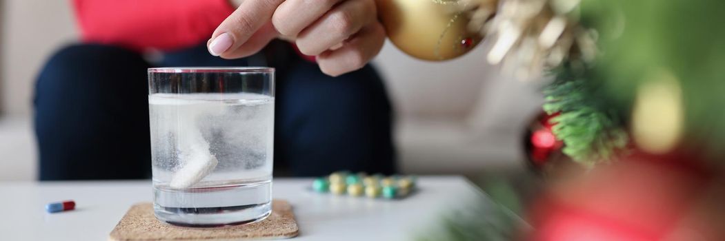 Close-up of female hand putting effervescent tablet in glass of water. Woman dissolving pill in water. Hangover and severe headache after party concept