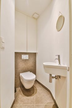 Modern flush toilet and ceramic sink installed on white tiled walls near mirror and towel in small restroom at home