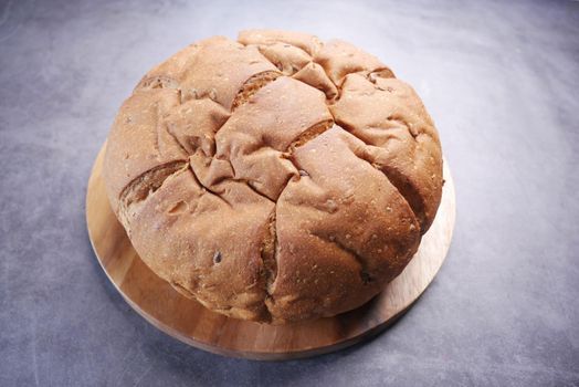top view of round brown baked bread on chopping board .