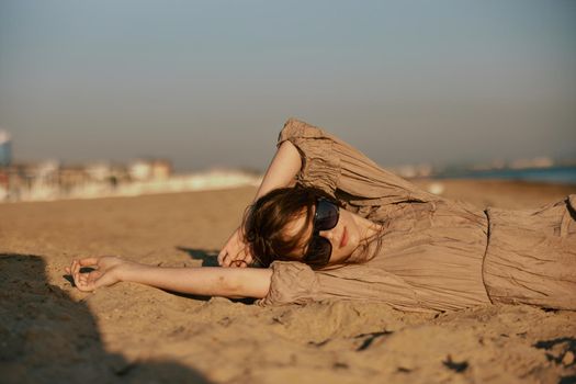 a woman in black sunglasses lies on the sand with her arms outstretched. High quality photo