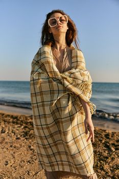 a woman wrapped in a plaid stands on the seashore in bright sunglasses. High quality photo