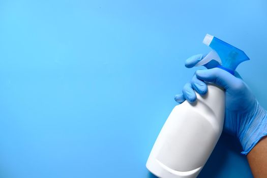 hand in blue rubber gloves holding spray bottle with copy space, top view