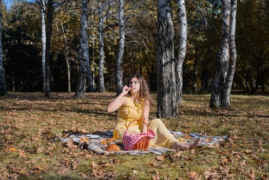 Leisure, free time. Beautiful caucasian woman in yellow dress on a picnic outdoors, sitting on a plaid in forest