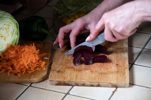 a woman cuts beets in the kitchen against the background of fresh vegetables, ingredients for step by step cooking soup. High quality photo