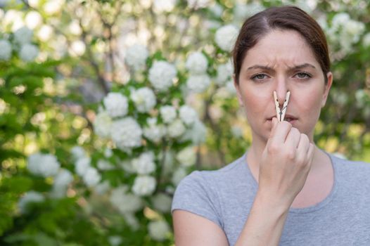 Caucasian woman with a clothespin on her nose on a walk in a blooming park