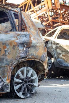 The car burned down completely, even the tires burned out. Burnt out car crash after fire. The bomb shell of the terrorist attack blew up civilians. Disaster zone. Abandoned car on the road