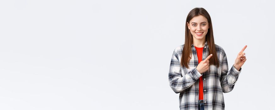 Lifestyle, different emotions, leisure activities concept. Friendly-looking attractive caucasian girl in checked shirt inform about new promos, pointing fingers right and smiling camera.