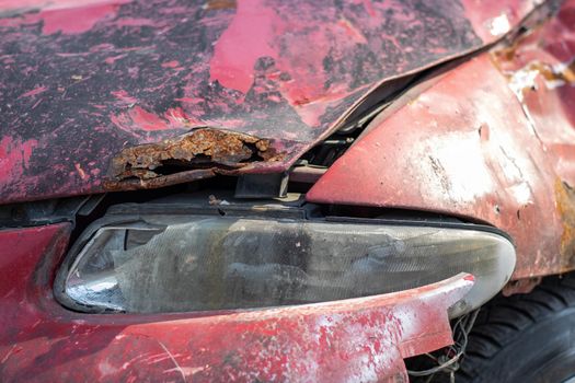 Broken headlights as a result of a collision. Broken red car after an accident. Car accident concept. Damaged emergency headlight, hood and bumper. Damage to the car body after the accident