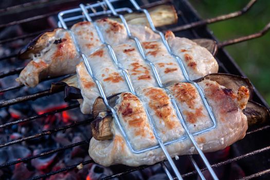 Grilled bacon-wrapped chicken tenders with lemon and rosemary on the grill wih grilled vegetables - peppers, and and eggplant.