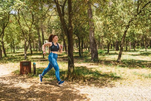young female athlete training, jogging in a public park to keep her body healthy. athlete practising sport outdoors. health and wellness lifestyle. outdoor public park, natural sunlight.