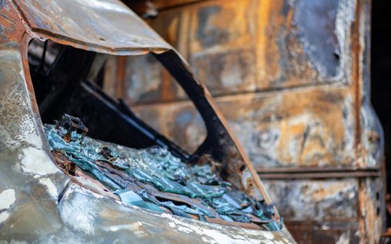 The car was completely destroyed by fire. Abandoned, burnt and rusty car by the road. Cars were on fire in the parking lot. War of Russia against Ukraine. Shrapnel and bullet holes in cars