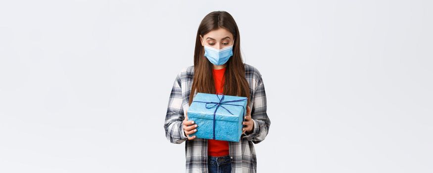 Covid-19, lifestyle, holidays and celebration concept. Happy and surprised birthday girl, employee receive present from coworkers, looking at wrapped gift with amazed grateful face in medical mask.