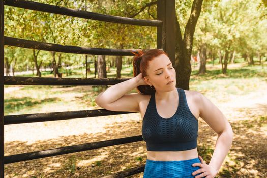 young female athlete, resting after training on an outdoor trellis. athlete practising outdoor sport. health and wellness lifestyle. outdoor public park, natural sunlight. vertical