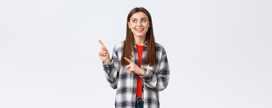 Lifestyle, different emotions, leisure activities concept. Dreamy cute smiling woman in checked shirt, pointing and looking upper left corner at best variant, picked or booked smth online.