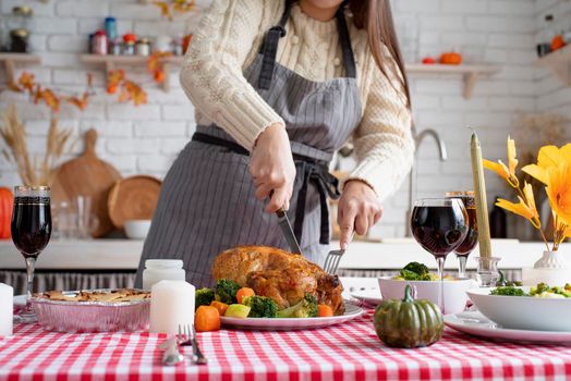 Thanksgiving day, autumn holidays. Woman in sweater and apron cutting turkey for family dinner in the kitchen, front view