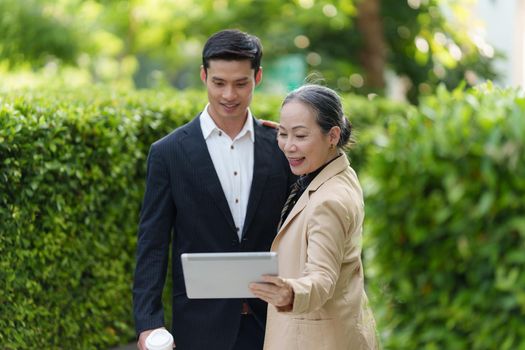 Portrait of Asian Senior Business woman and young business man discussing about project by digital tablet. Account and Finance concept