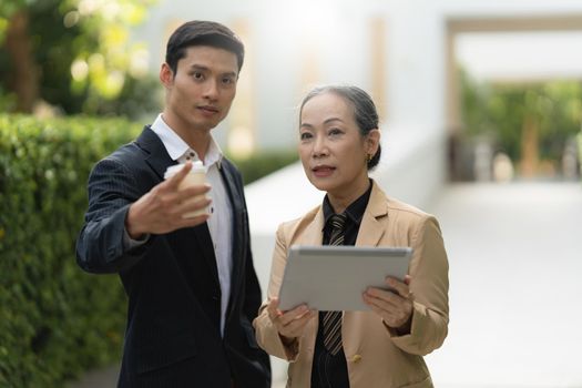 Portrait of Asian Senior Business woman and young business man discussing about project by digital tablet. Account and Finance concept