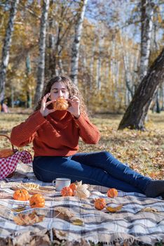 Leisure, free time. Beautiful caucasian woman in red sweater on a picnic outdoors, sitting on a plaid in autumn forest