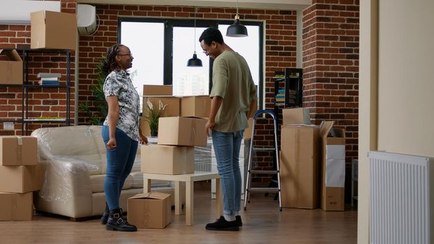 Husband and wife moving in new home with carton boxes, using furniture to start new beginnings together in living room. Holding packages in rented property on loan for relocation.