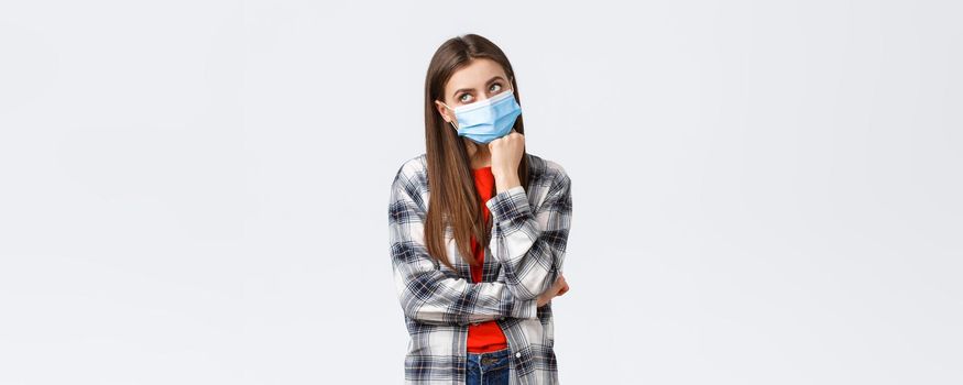 Coronavirus outbreak, leisure on quarantine, social distancing and emotions concept. Thoughtful and gloomy young woman hate staying home self-isolation, dreaming go vacation, wear medical mask.