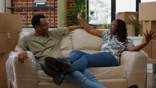 Married partners taking break on couch after moving in new real estate property, relaxing on sofa. Unpacking furniture and decorating apartment room, homeowners bought house on loan.