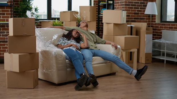 African american partners unpacking living room couch and furniture after moving in new household property. Taking break from interior decoration, on moving day for new beginnings.