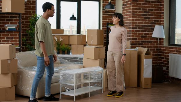 Diverse couple moving in together and unpacking furniture in new home, feeling happy about house relocation investment. New beginnings in apartment flat bought on mortgage and loan.
