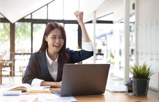 Happy young asian businesswoman sitting on her workplace in the office. Young woman working at laptop in the office..