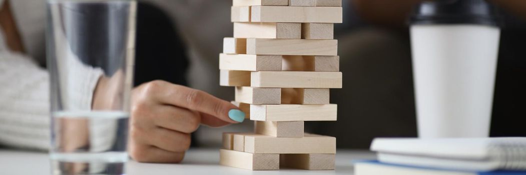 Close-up of womans hand pull one of wooden blocks from high build tower. Friends or colleagues play board game for fun. Entertainment, spare time concept