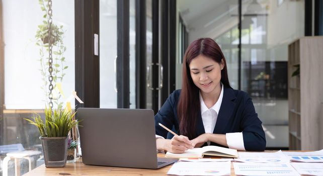 Happy young asian businesswoman sitting on her workplace in the office. Young woman working at laptop in the office..