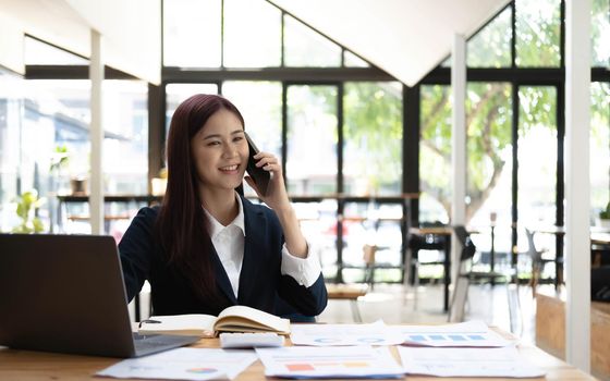 Asian woman talking on the phone and working on a laptop with a smiling face, Business Cell Phone Conversations, Working at cafe, cafe lifestyle, Stay cafe, New normal, learning, Social distancing..