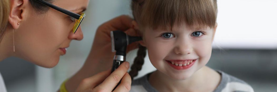 Portrait of little girl smile while doctor examine ears with special instrument. Calm kid not afraid of doctors and hospital. Checkup, pediatrician concept