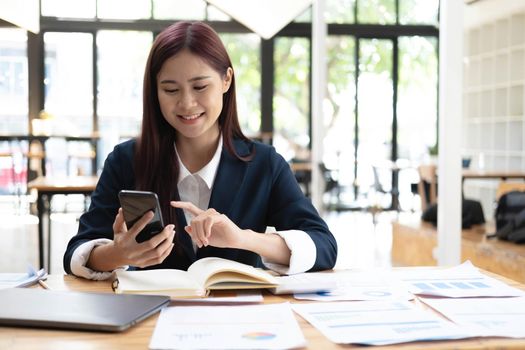 Portrait of young asian business woman talk on smartphone write notebook laptop in home office. Beautiful girl at desk computer take home order. Startup business asia woman online sme telemarketing..