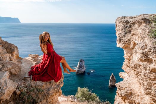 A girl with flowing hair in a long red dress sits on a rock above the sea. The stone can be seen in the sea