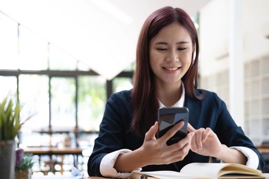 Asian woman talking on the phone and working on a laptop with a smiling face, Business Cell Phone Conversations, Working at cafe, cafe lifestyle, Stay cafe, New normal, learning, Social distancing..