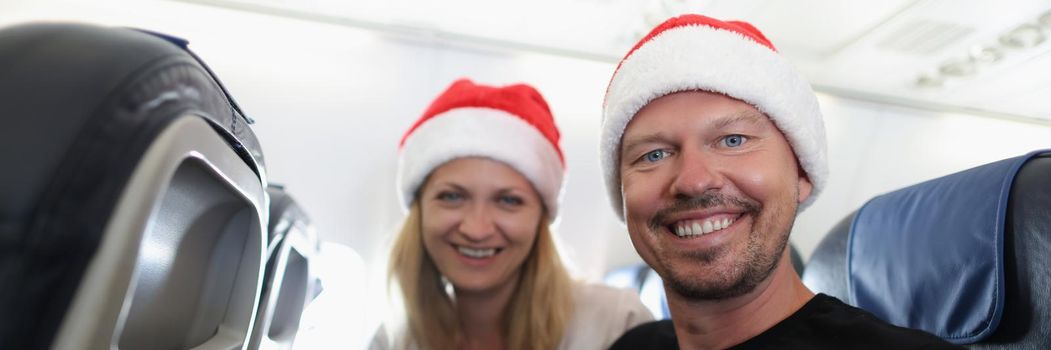 Portrait of cheerful woman and man on flight high in air smile and wear festive hats. Meet and celebrate new year in sky. Holiday, festive, couple concept