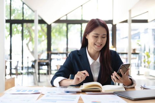 Asian woman talking on the phone and working on a laptop with a smiling face, Business Cell Phone Conversations, Working at cafe, cafe lifestyle, Stay cafe, New normal, learning, Social distancing..