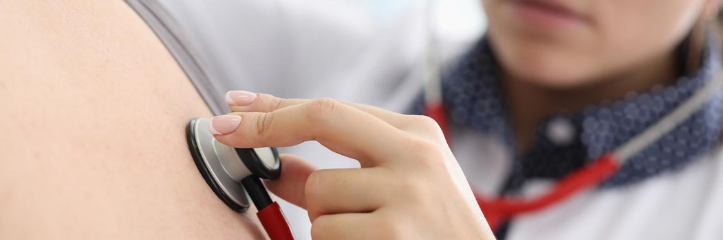 Close-up of young female doctor listen to patients back with stethoscope tool. Concentrated intern examine body, diagnostic in clinic. Medicine concept