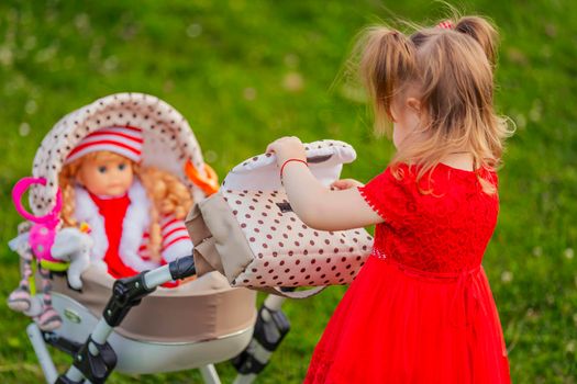 girl plays with her doll who is sitting in a toy stroller