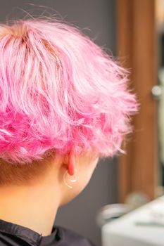 Back view of pink hairstyle of young woman after dyeing hair and making highlights in beauty salon