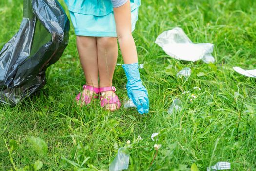 Little girl cleans plastic trash on the green grass in the park