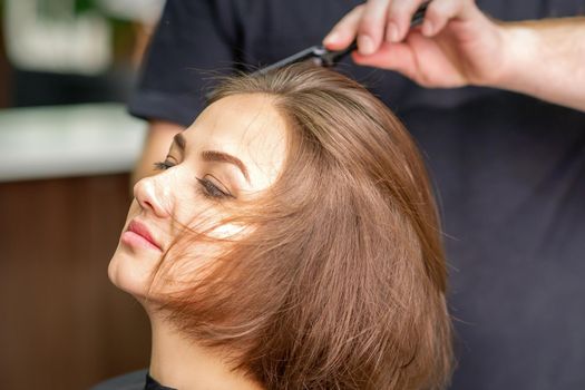 Hand of hairdresser combs hair of young caucasian woman in beauty salon.
