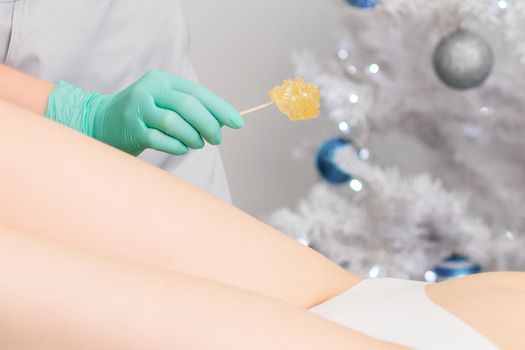 Young woman getting wax epilation of legs. Depilation concept. Product waxing bowl. Christmas discount waxing