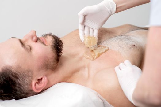 Epilation chest of young male with liquid wax paste by hands of female cosmetologist in beauty salon