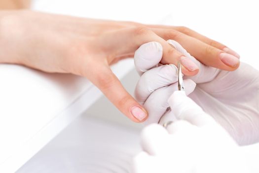 Close up of manicurist using manicure scissors to remove cuticle of female nails in manicure salon