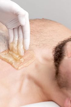 Epilation chest of young male with liquid wax paste by hands of female cosmetologist in beauty salon