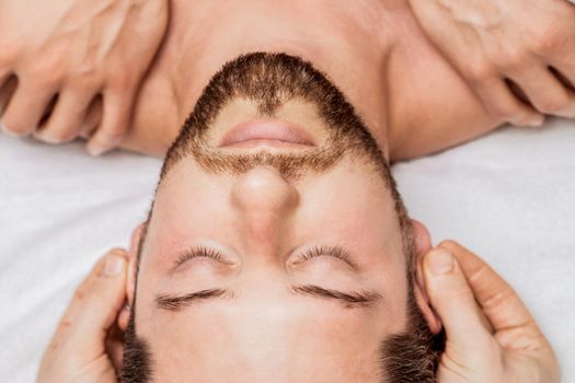 Man receiving relaxing head massage by massage therapist hands, top view.