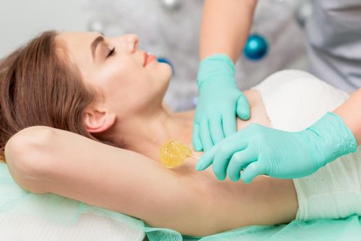 Epilation armpit of young woman by beautician close up.